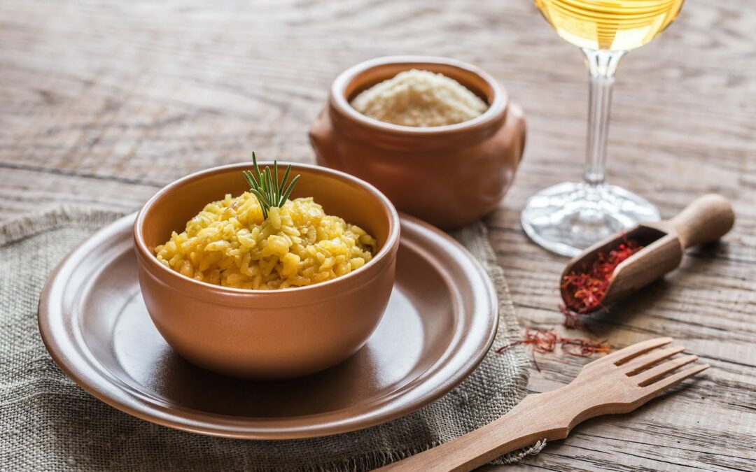 Piatto di risotto alla milanese con posate e bicchieri.