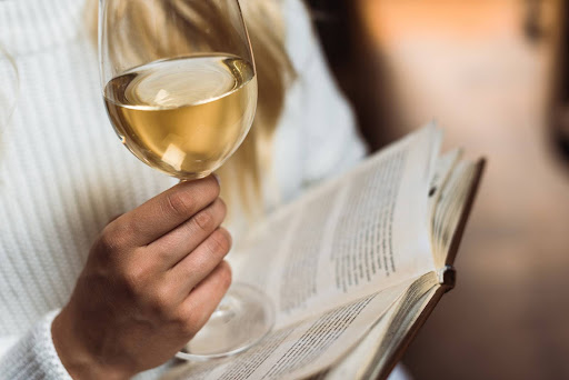 Ragazza che tiene con una mano un calice di vino bianco e con l'altra un libro.